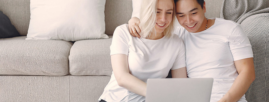 Couple sitting in front of couch looking at laptop